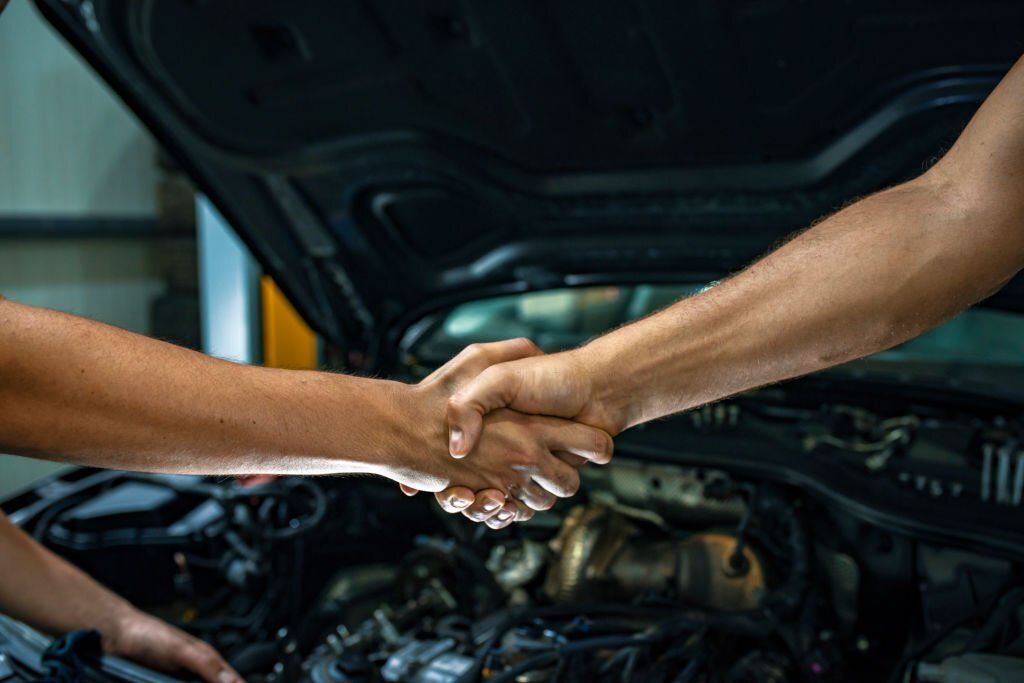Caucasian young mechanic shaking hands with a mature male customer in front of a car. Photo of a man giving an handshake in an industrial facility. Man greets auto master. Concept - car service. Handshake.